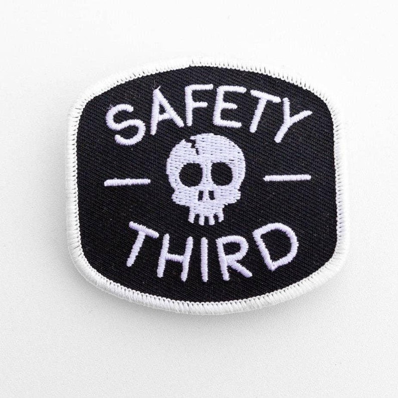 Close on white stitching, the black Safety Third patch shows its skull and white border on a pale surface.