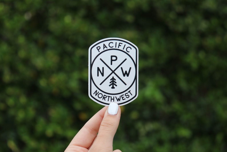 Held a little farther back against a leafy hedge, the black and white PNW Compass sticker fills the frame.