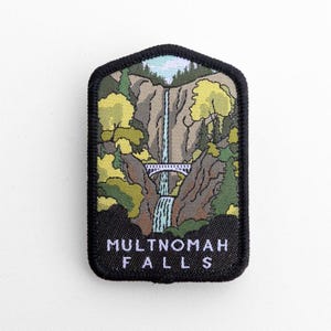 Peut inclure: Un écusson brodé rectangulaire à bordure noire représentant le paysage des chutes de Multnomah. Le motif comprend une haute cascade, un pont voûté blanc, des arbres verts et jaunes, et des falaises rocheuses. Le texte MULTNOMAH FALLS est en blanc.