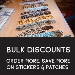 May include: A variety of stickers and patches featuring different designs, including a Big Sur California sticker, a warning sign sticker, and a camping sticker. The text "BULK DISCOUNTS" is displayed in white on a black background. The text "ORDER MORE, SAVE MORE ON STICKERS & PATCHES" is displayed in white on a black background.