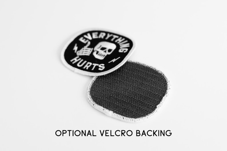 May include: A round embroidered patch with a black background and white border. The design features a white skull, a skeletal hand giving a thumbs up, and the text EVERYTHING HURTS. A second patch shows a dark gray hook-and-loop velcro backing.