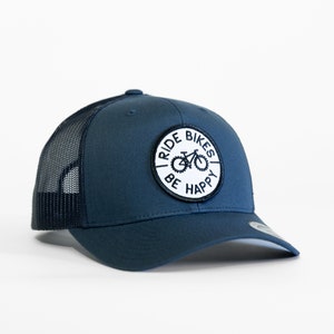 May include: A navy blue trucker hat with a white patch that says "Ride Bikes Be Happy" and a black silhouette of a bicycle.