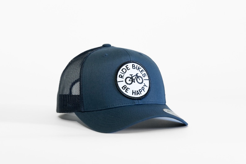 May include: A navy blue trucker hat with a white patch that says "Ride Bikes Be Happy" and a black silhouette of a bicycle.