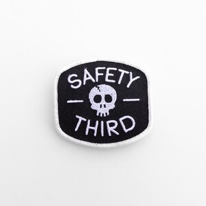 Centered on a plain white background, the small Safety Third patch shows its skull between two dashes.