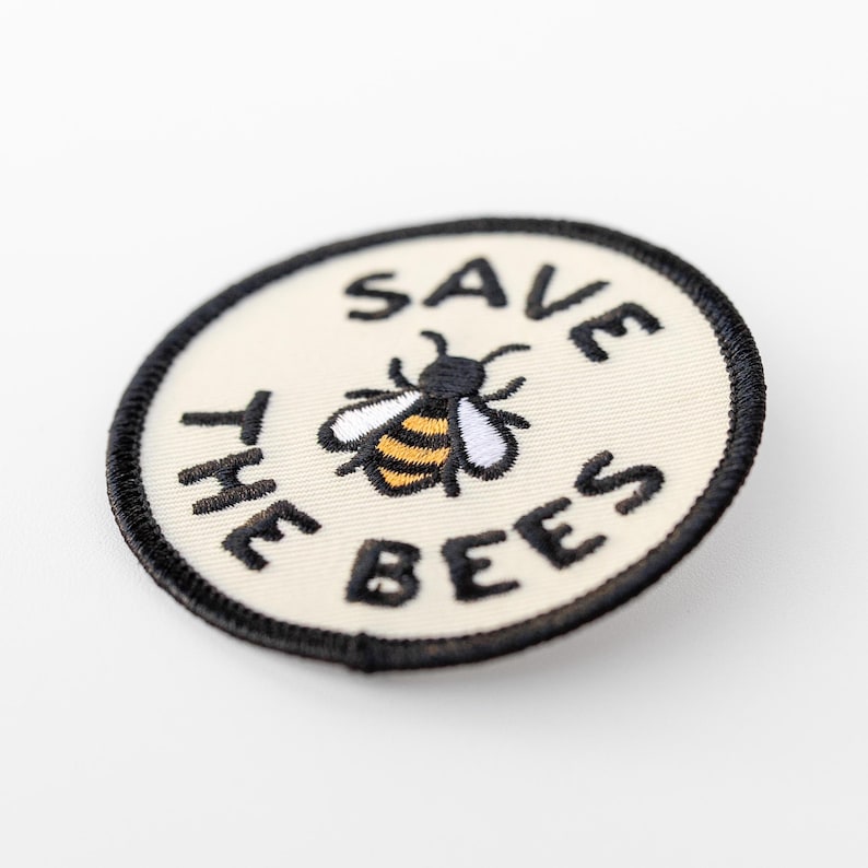 Tilted slightly to one side, the Save The Bees patch catches the light across its stitched border and striped bee body.