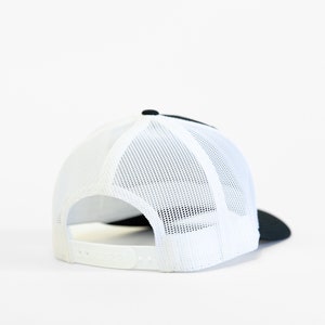 May include: A black and white trucker hat with a mesh back. The hat is turned to show the back of the hat.