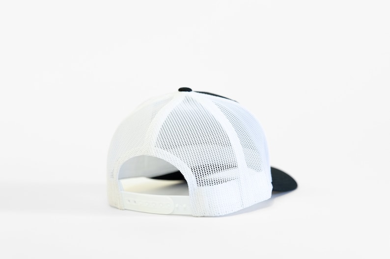 May include: A black and white trucker hat with a mesh back. The hat is turned to show the back of the hat.