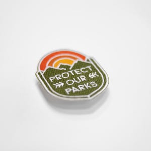Tilted at an angle on a bright white surface, the small Protect Our Parks patch catches light along its edge.