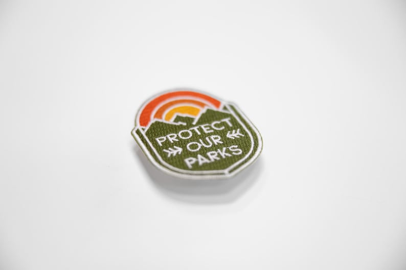 Tilted at an angle on a bright white surface, the small Protect Our Parks patch catches light along its edge.
