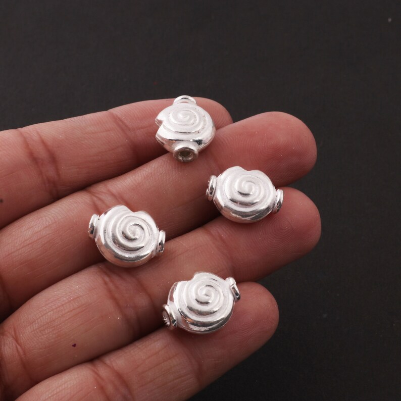 May include: Four silver-toned metal beads with a spiral design. The beads are smooth and have a shiny finish.