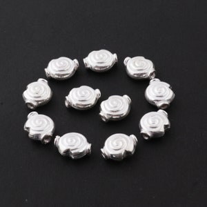 May include: Twelve silver-toned metal beads with a spiral design. The beads are oval-shaped and have a hole through the center for stringing.