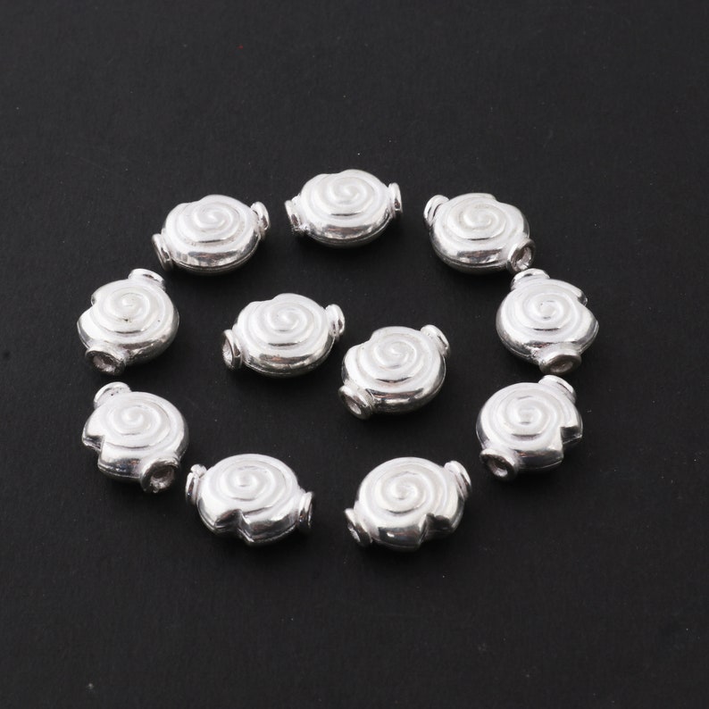 May include: Twelve silver-toned metal beads with a spiral design. The beads are oval-shaped and have a hole through the center for stringing.