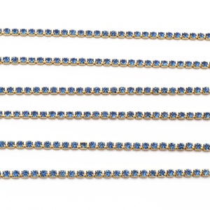 May include: Five rows of light blue rhinestone chain trim. The chain is made of small, square-shaped rhinestones connected by gold metal.