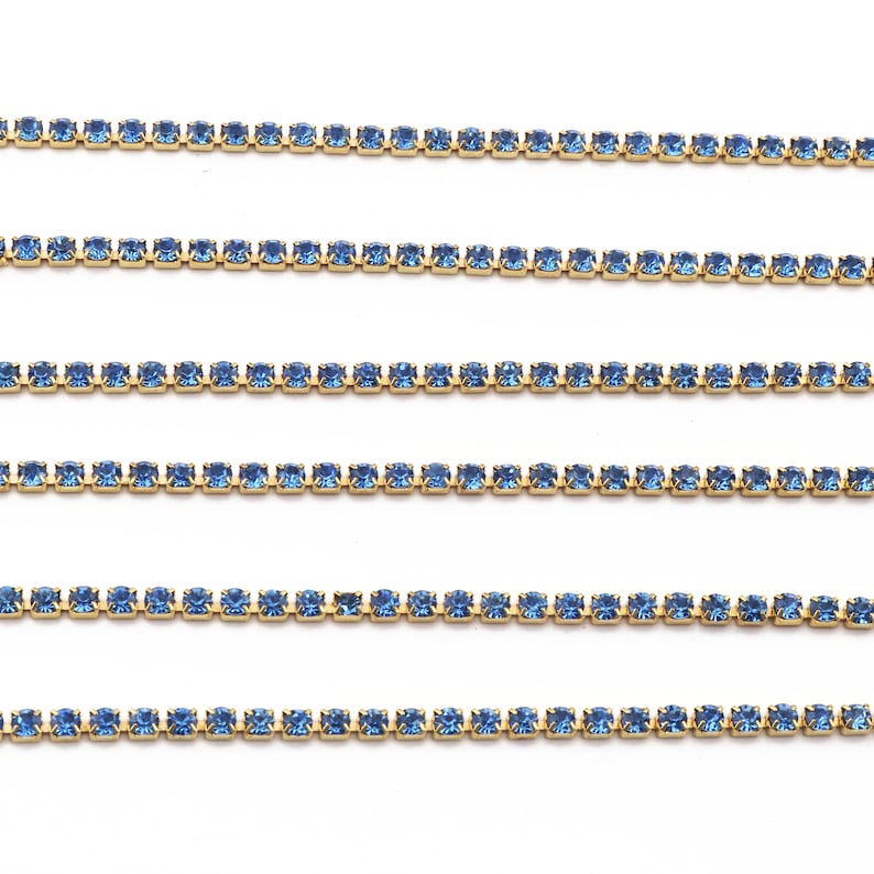 May include: Five rows of light blue rhinestone chain trim. The chain is made of small, square-shaped rhinestones connected by gold metal.