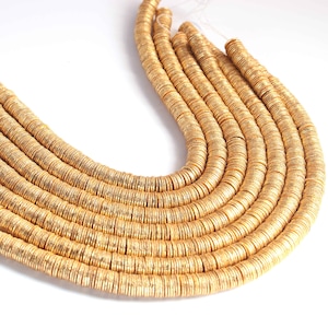 Peut inclure: Un brin de perles en métal de couleur dorée, chaque perle est un disque plat avec une surface texturée. Les perles sont disposées en cercle, créant un aspect de collier.