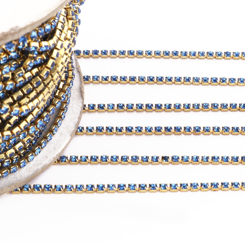 May include: A spool of gold chain with blue square rhinestones. The chain is laid out in rows on a white surface.