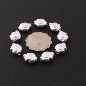 May include: Ten silver-colored metal beads in the shape of a spiral. The beads are arranged in a circle around a two dollar coin from Singapore.