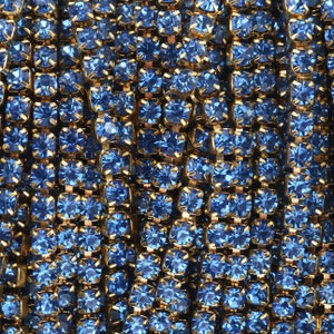 May include: A close-up of a chain made of small, blue, square-shaped rhinestones connected by gold metal links.