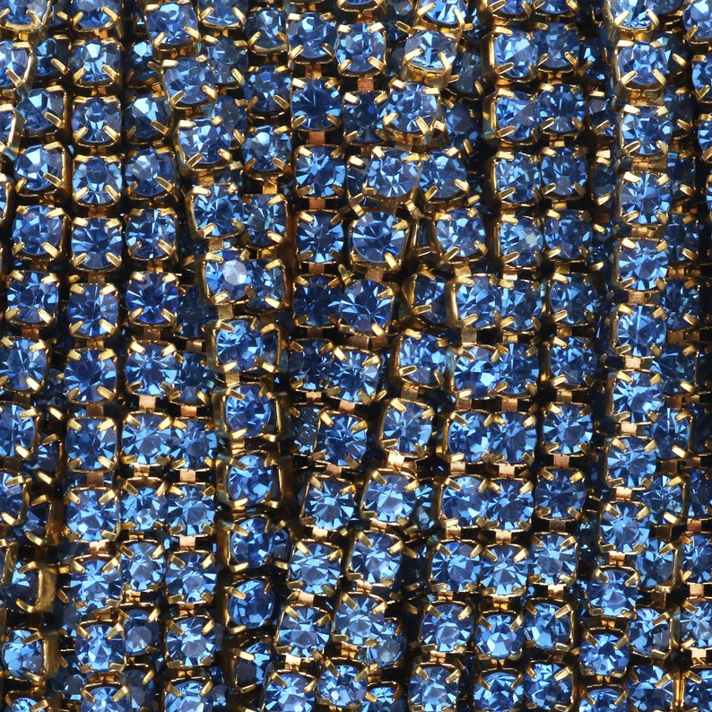 May include: A close-up of a chain made of small, blue, square-shaped rhinestones connected by gold metal links.