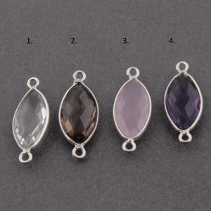 Puede incluir: Cuatro abalorios ovalados de piedra preciosa con lazos de metal plateado. Las piedras preciosas son transparentes, marrón ahumado, rosa claro y morado.