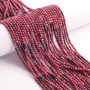 Può includere: Un filo di piccole perle di rubino rosso sfaccettate. Le perle sono di dimensioni uniformi e hanno una forma leggermente irregolare. Il filo è lungo circa 40 cm.