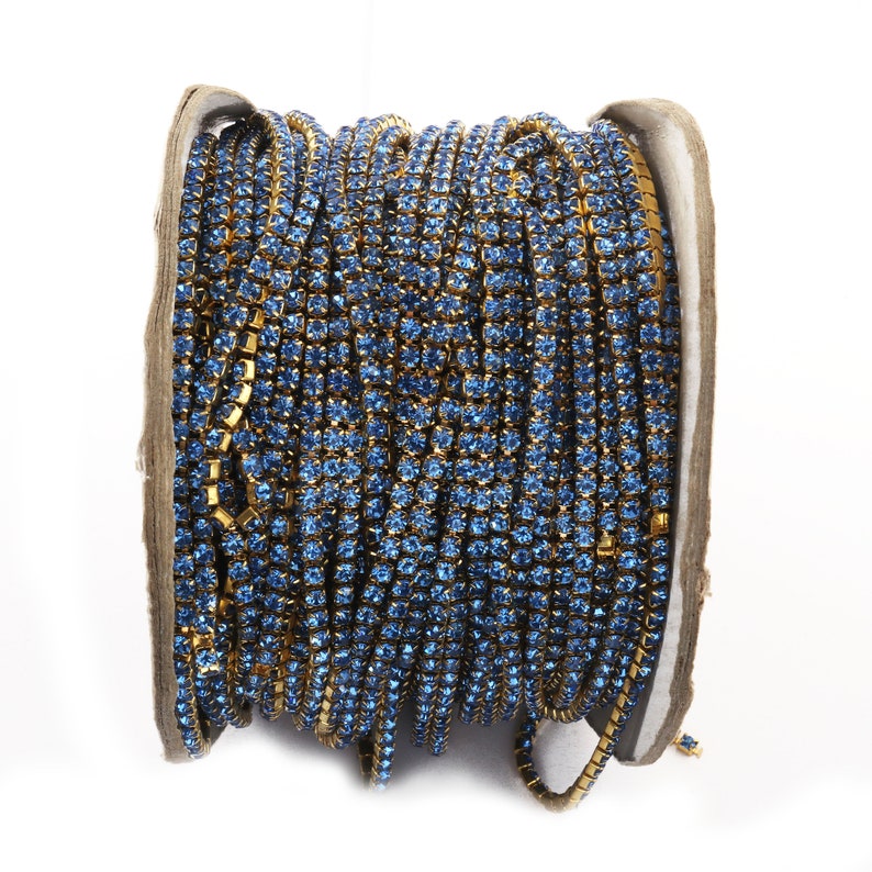 May include: A spool of blue rhinestone trim with gold metal settings. The trim is wound around a cardboard spool.