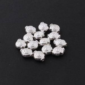 May include: A group of silver-toned metal beads with a spiral design. The beads are arranged in a loose pile on a black surface.
