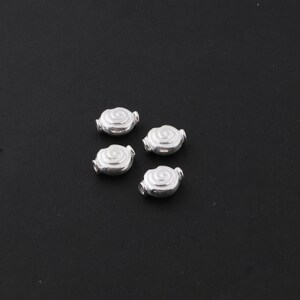 May include: Four silver-toned metal beads with a spiral design. The beads are oval-shaped and have a smooth, shiny finish.