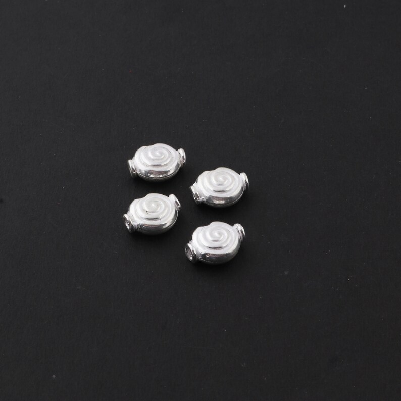 May include: Four silver-toned metal beads with a spiral design. The beads are oval-shaped and have a smooth, shiny finish.