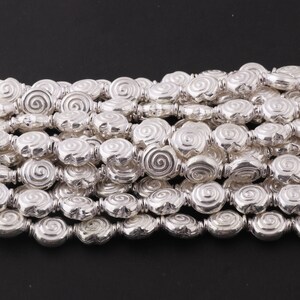 May include: A strand of silver-toned beads with a spiral design. The beads are oval-shaped and have a textured surface.