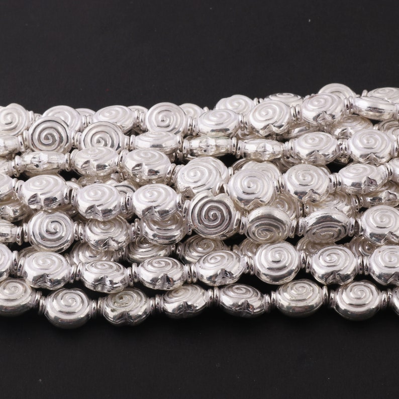 May include: A strand of silver-toned beads with a spiral design. The beads are oval-shaped and have a textured surface.