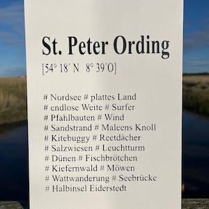 Könnte beinhalten: Ein weißes Schild mit schwarzem Text, auf dem steht: "St. Peter Ording [54° 18′N 8° 39′O] # Nordsee # plattes Land # endlose Weite # Surfer # Pfahlbauten # Wind # Sandstrand # Maleens Knoll # Kitebuggy # Reetdächer # Salzwiesen # Leuchtturm # Dünen # Fischbrötchen # Kiefernwald # Möwen # Wattwanderung # Seebrücke # Halbinsel Eiderstedt"