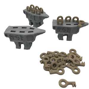 May include: Three gray metal anvils with a series of small gold rings on top. The anvils have a raised design of runes on the side. A pile of small gold keys are scattered in front of the anvils.