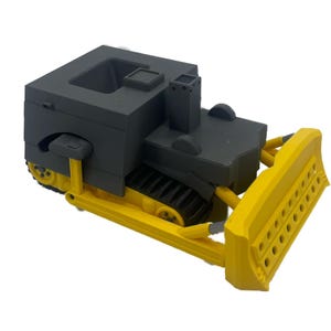 May include: A toy bulldozer with a gray cab and yellow blade. The bulldozer has a black track and a black exhaust pipe.