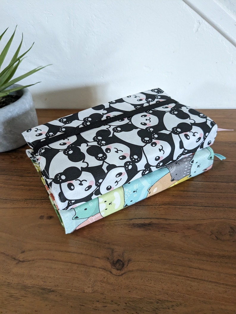 Puede incluir: Dos estuches de l&aacute;pices de tela apilados uno encima del otro. El estuche superior es blanco y negro con un patr&oacute;n de oso panda. El estuche inferior es multicolor con una variedad de patrones de animales.