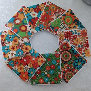 Puede incluir: Un conjunto de posavasos cuadrados de tela con un dise&ntilde;o floral retro. Los posavasos presentan una variedad de colores vibrantes, incluyendo naranja, azul, verde y blanco. Los dise&ntilde;os florales recuerdan a los a&ntilde;os 70.
