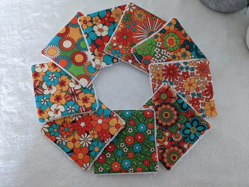 Puede incluir: Un conjunto de posavasos cuadrados de tela con un dise&ntilde;o floral retro. Los posavasos presentan una variedad de colores vibrantes, incluyendo naranja, azul, verde y blanco. Los dise&ntilde;os florales recuerdan a los a&ntilde;os 70.