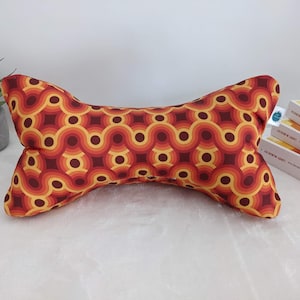 Puede incluir: Una almohada de cuello con estampado rojo, naranja y amarillo con un diseño de onda. La almohada tiene forma de hueso y está hecha de tela.