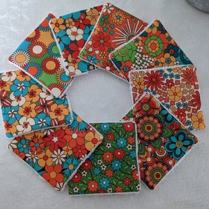 Puede incluir: Un conjunto de posavasos cuadrados de tela con estampados florales en tonos naranja, azul, verde y blanco. Los posavasos est&aacute;n dispuestos en forma circular, mostrando sus dise&ntilde;os vibrantes y bordes blancos suaves. Ideales para a&ntilde;adir un toque retro a cualquier hogar.