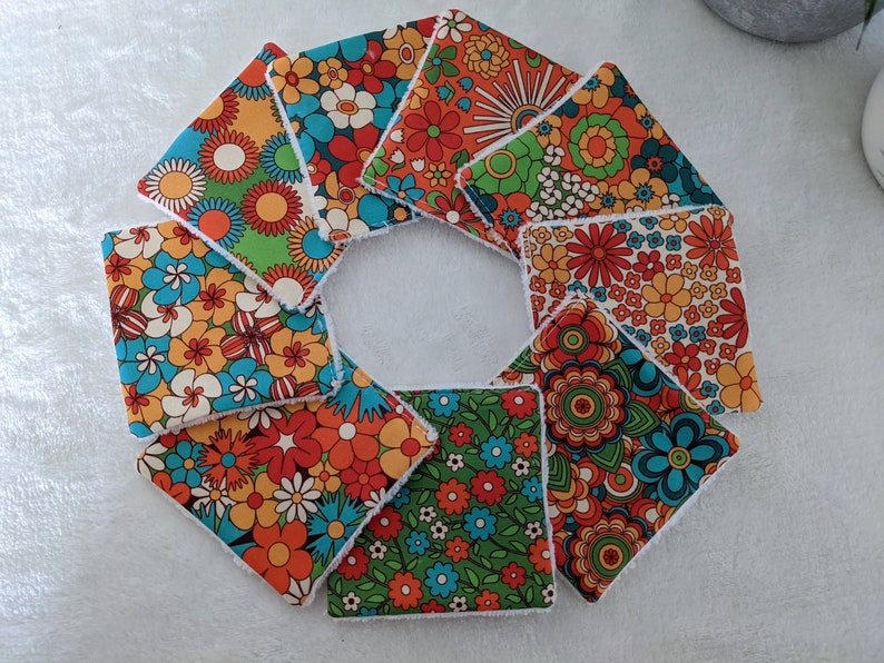 Puede incluir: Un conjunto de posavasos cuadrados de tela con estampados florales en tonos naranja, azul, verde y blanco. Los posavasos est&aacute;n dispuestos en forma circular, mostrando sus dise&ntilde;os vibrantes y bordes blancos suaves. Ideales para a&ntilde;adir un toque retro a cualquier hogar.