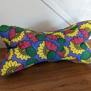 May include: A purple, yellow, green, and pink patterned pillow with a bow tie shape. The pillow is made of fabric with a floral design.
