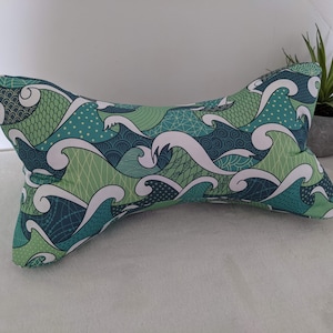May include: A green and blue patterned pillow with a wave design. The pillow is shaped like a bone and is made of soft fabric.