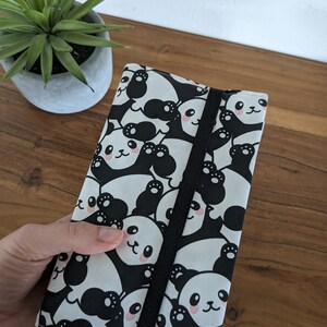 Puede incluir: Una funda para cuaderno con estampado de panda en blanco y negro con cierre el&aacute;stico negro. La funda est&aacute; hecha de tela y tiene un marcap&aacute;ginas de cinta rosa.