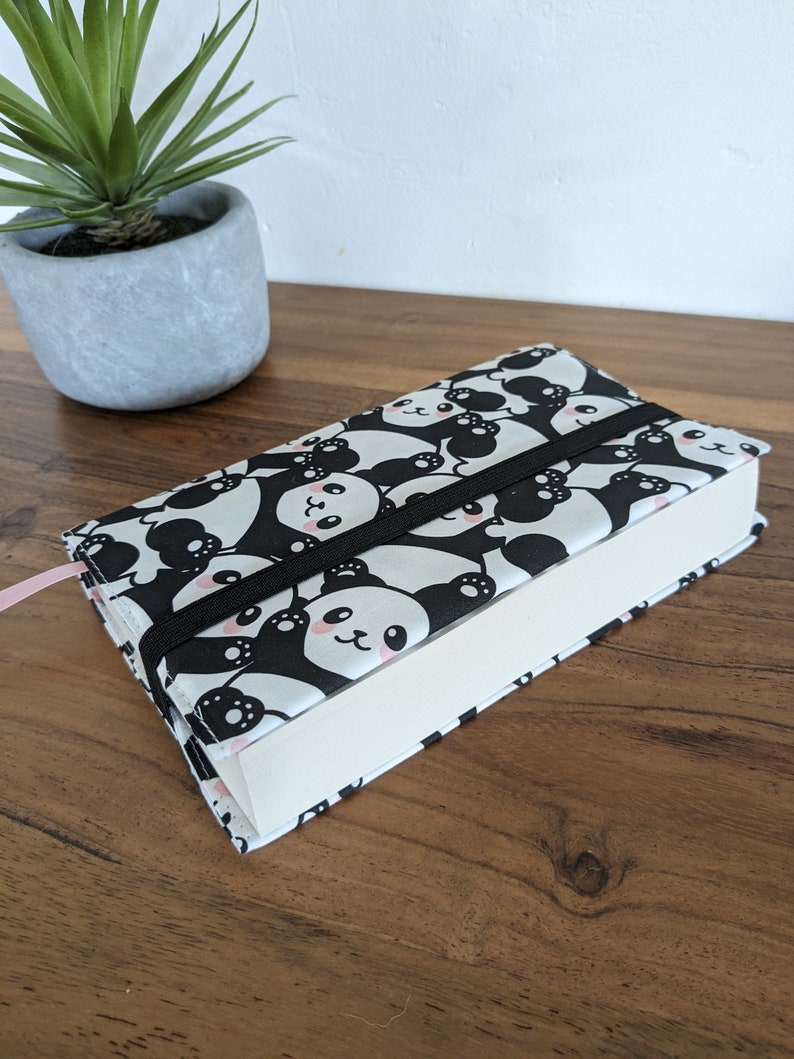 Puede incluir: Una cubierta de libro blanca y negra con un patr&oacute;n de panda. La cubierta tiene una banda el&aacute;stica negra.