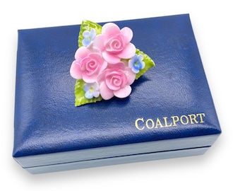 May include: A pink and white porcelain flower brooch in a blue box with the word "COALPORT" printed on the box.