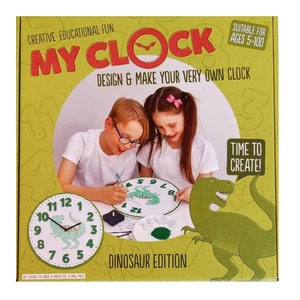 May include: A box for a dinosaur-themed clock making kit. The box features a green dinosaur, two children, and a clock face with a dinosaur design. The text on the box reads "My Clock, Design & Make Your Very Own Clock, Dinosaur Edition, Suitable for Ages 5-100, Time to Create!"