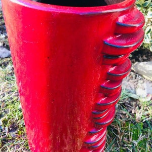 Könnte beinhalten: Eine rote Keramikvase mit einem strukturierten, gewellten Design. Die Vase ist hoch und zylindrisch.