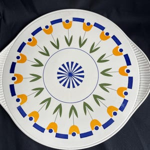 Könnte beinhalten: Weiße Keramik-Servierplatte mit einem blauen, gelben und grünen Blumendesign. Die Platte hat einen erhöhten Rand und einen gewellten Rand.