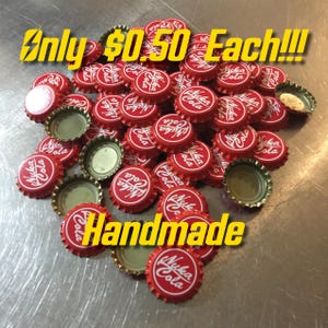 May include: A pile of red bottle caps with gold rims and the words "Nuka Cola" printed in white. The caps are handmade and are priced at £0.50 each.