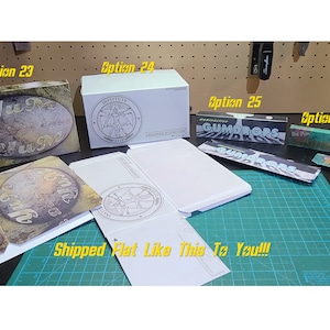 May include: Four flat-packed boxes, ready to be assembled. The boxes are labeled with the words "Yum", "Institute", "GUMDROPS", and "The Pops". The boxes are on a green cutting mat.